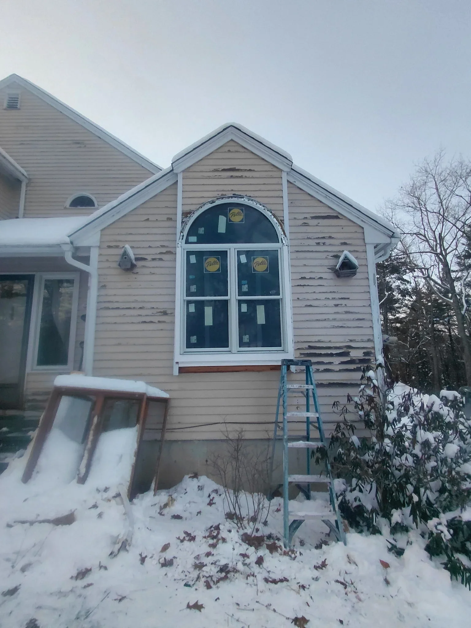 Home exterior with new white trim around arched window and restored siding in winter