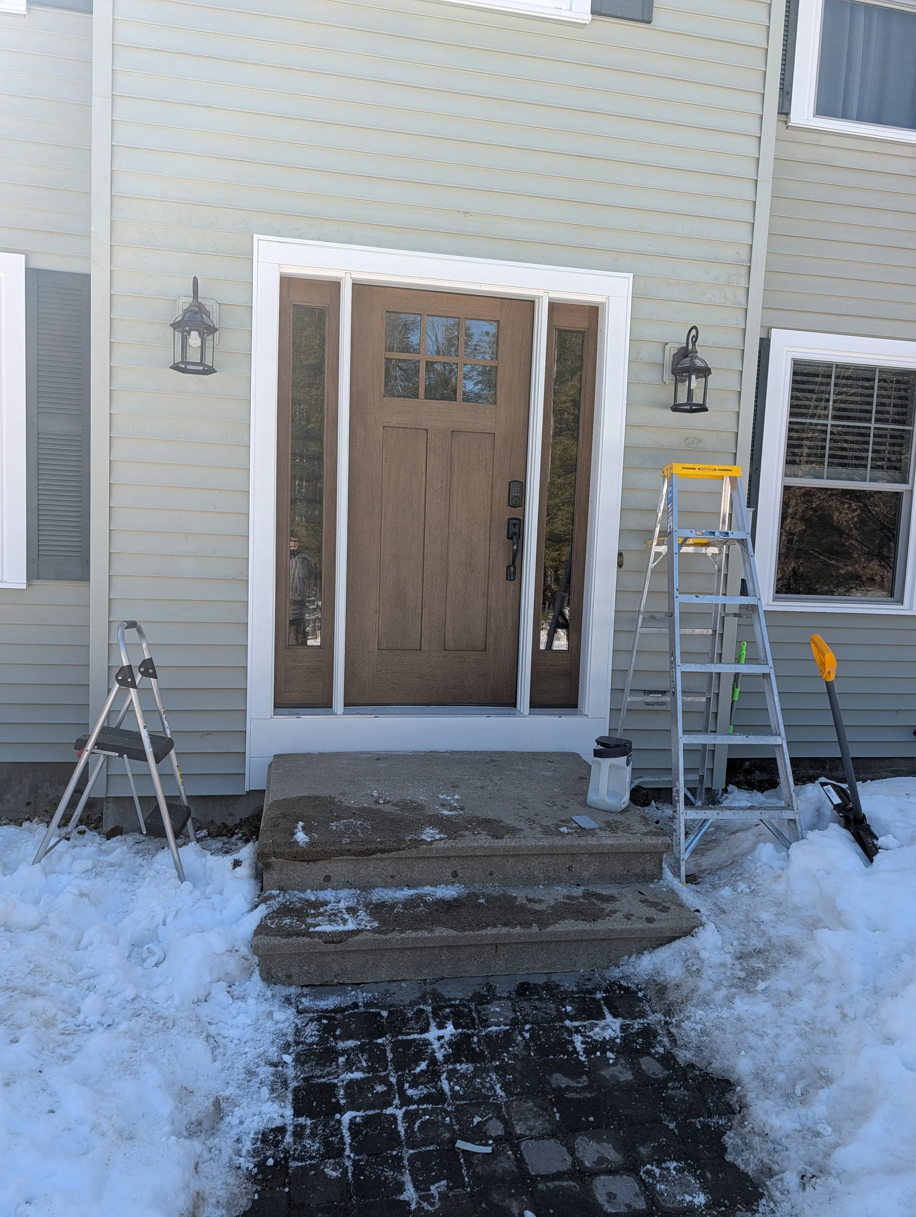 Brown fiberglass entry door with white trim and glass sidelights on vinyl-sided home