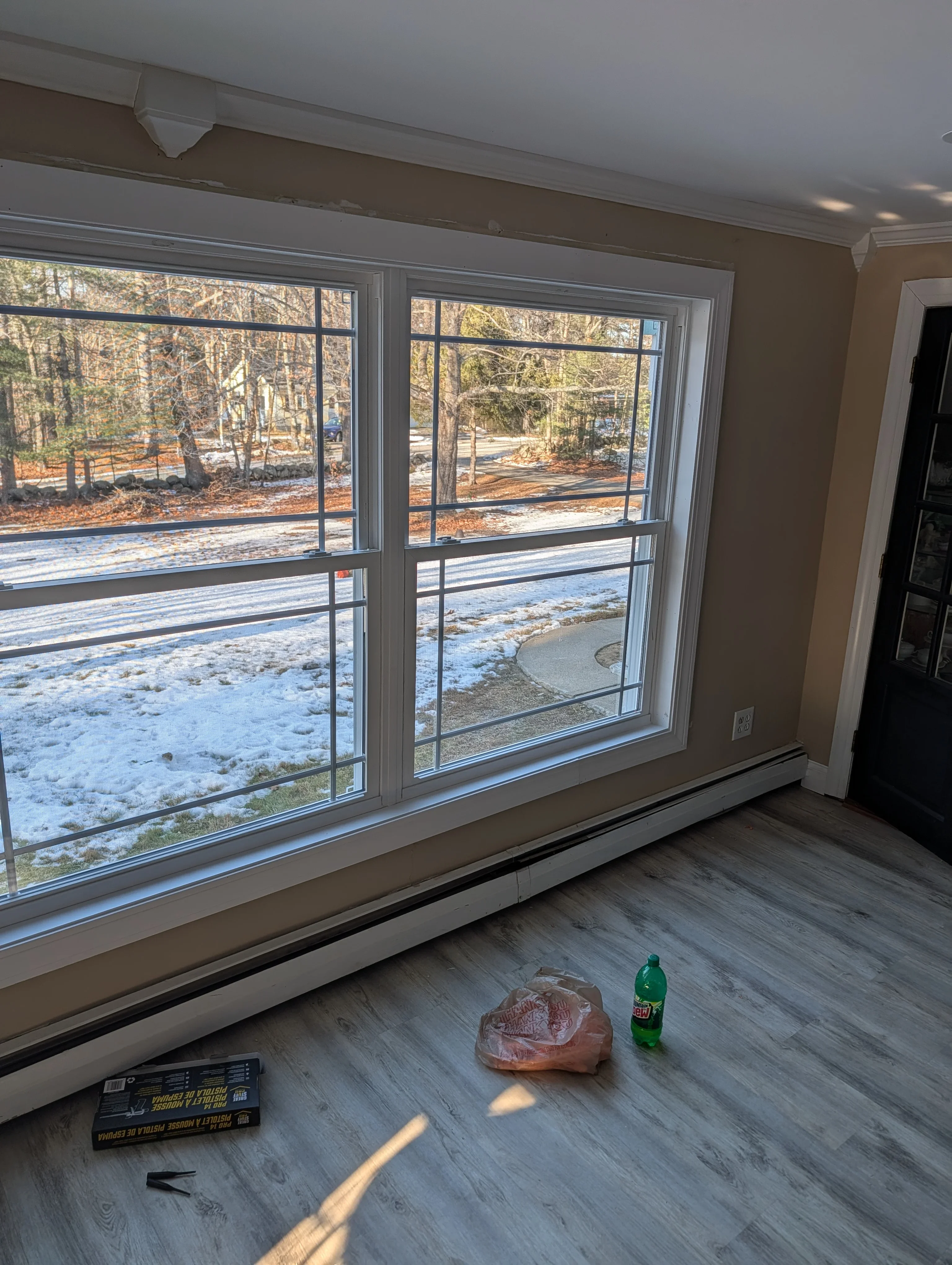 Two large white vinyl windows with horizontal grids overlooking snowy wooded property