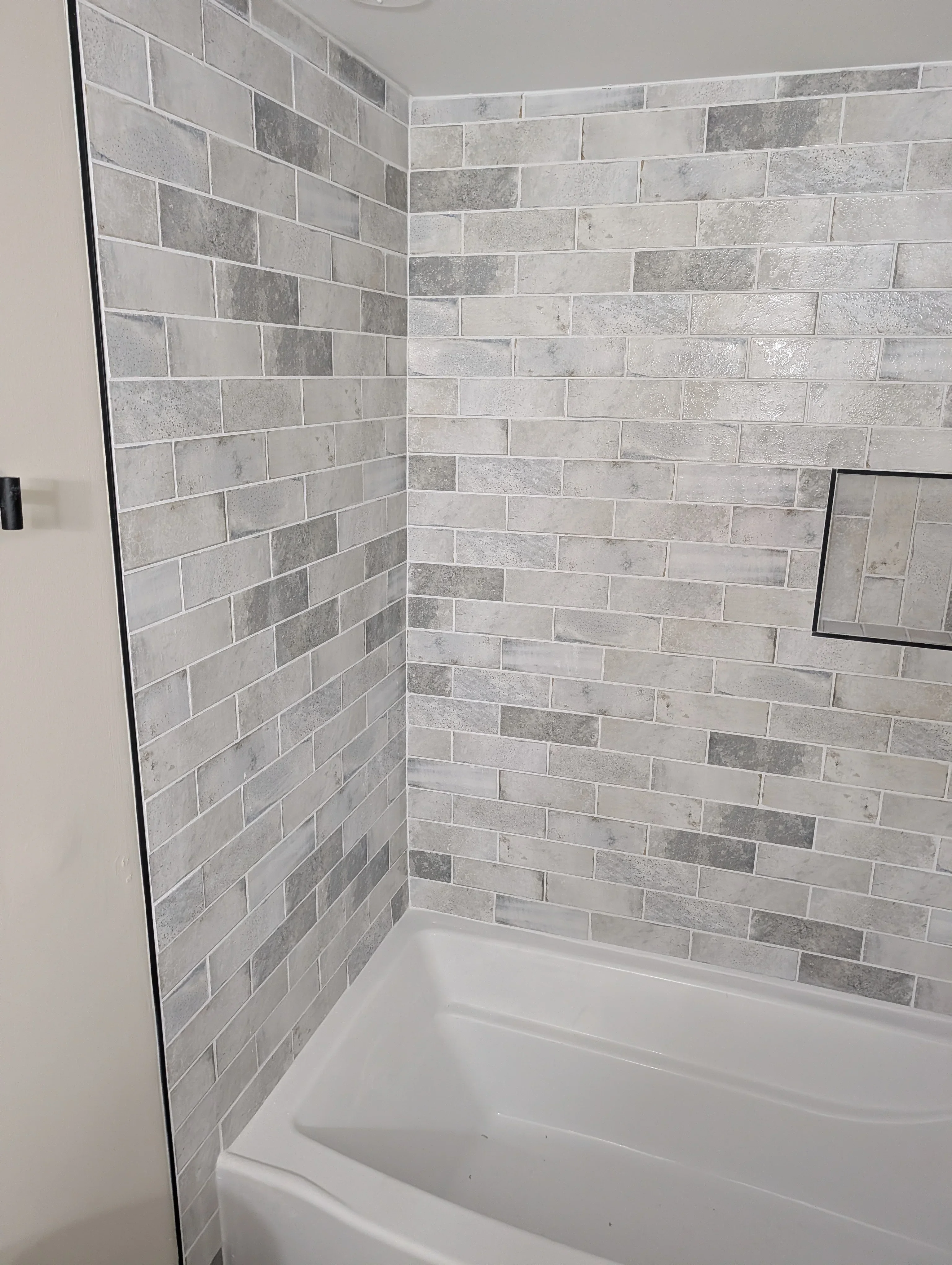 Gray and white subway tile shower surround with staggered brick pattern and white tub