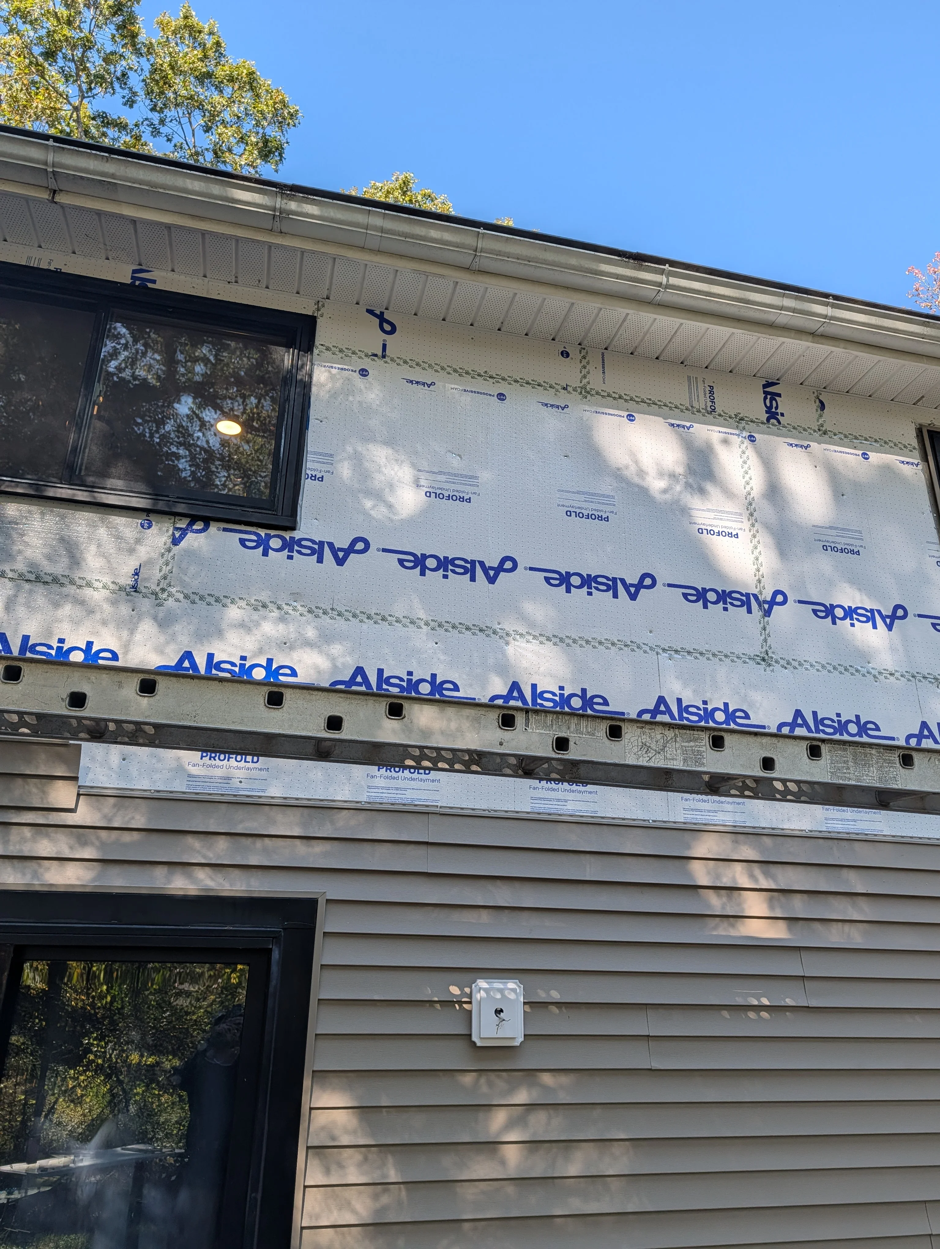 Residential roof with white underlayment and blue Alside barrier installed during construction phase