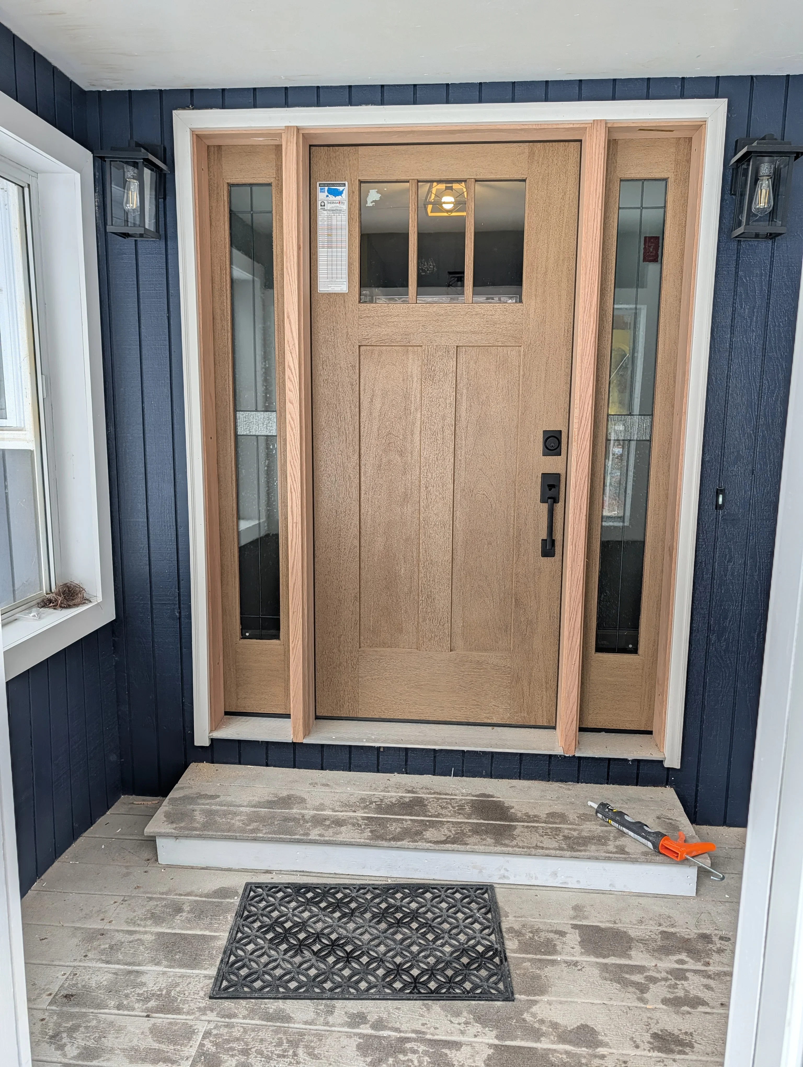 Natural oak entry door with sidelights and glass panes on navy siding