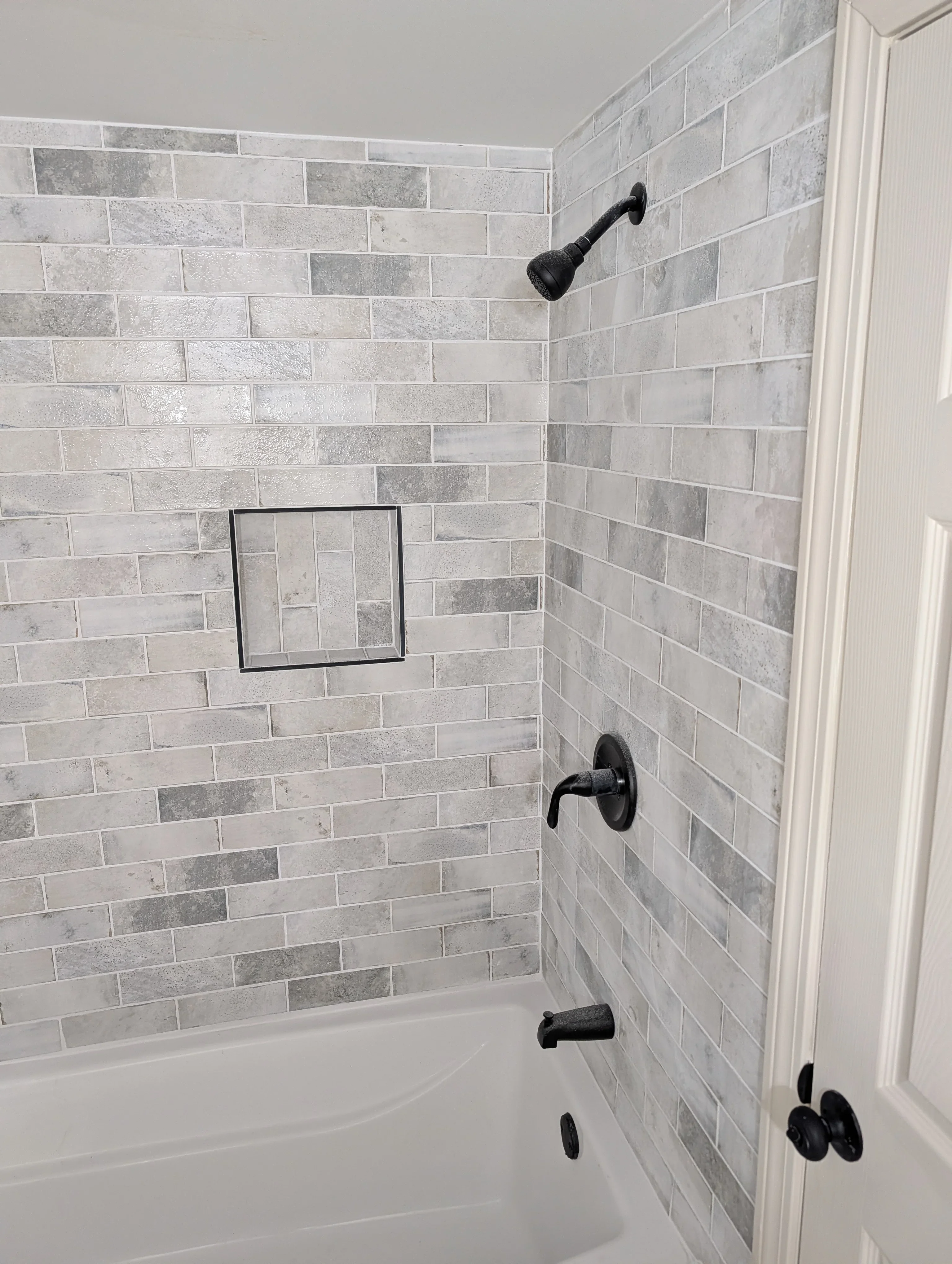 Gray and white subway tile shower with black fixtures and recessed niche