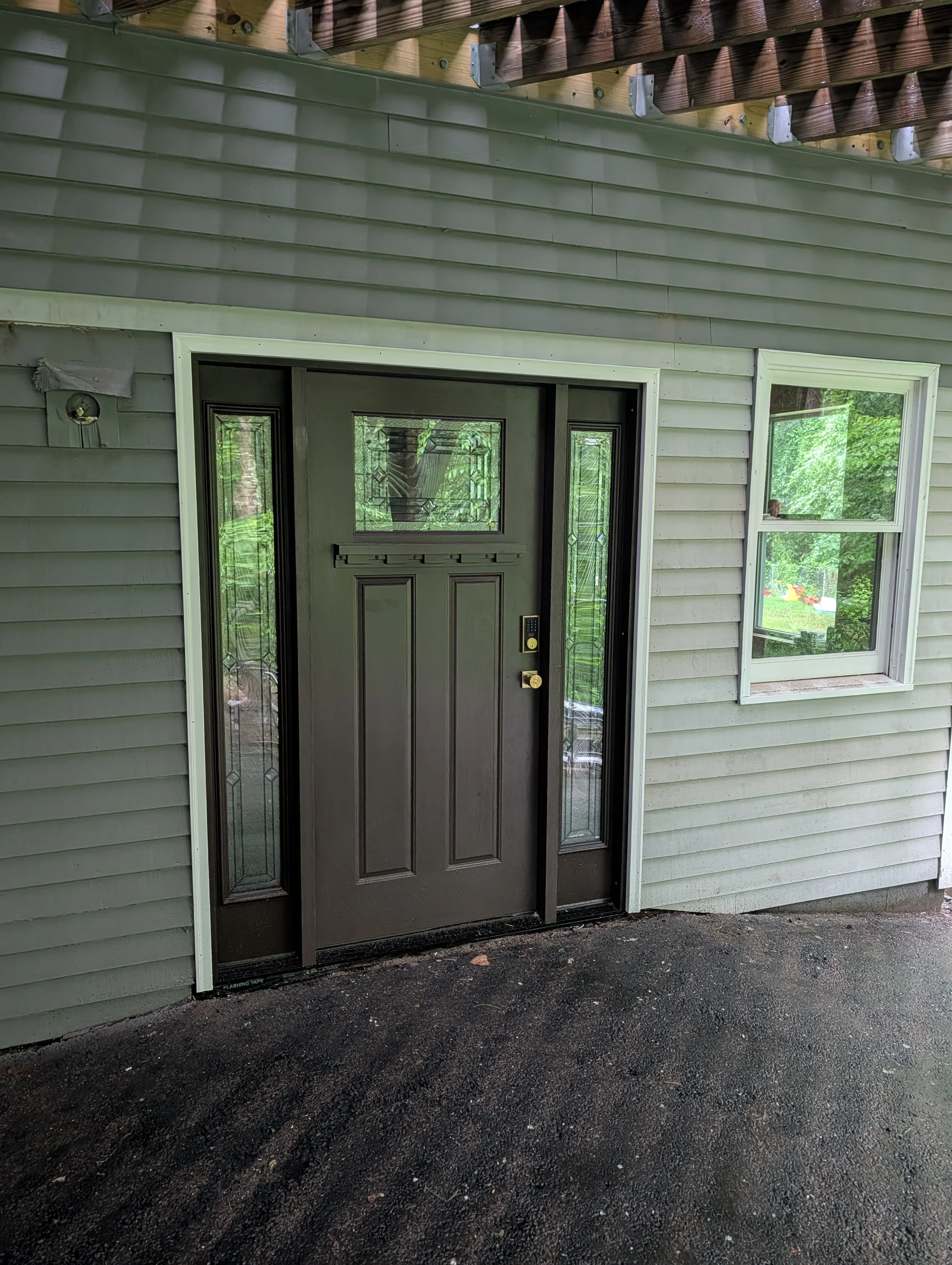 Dark entry door with sidelights and leaded glass panels installed on green vinyl-sided home