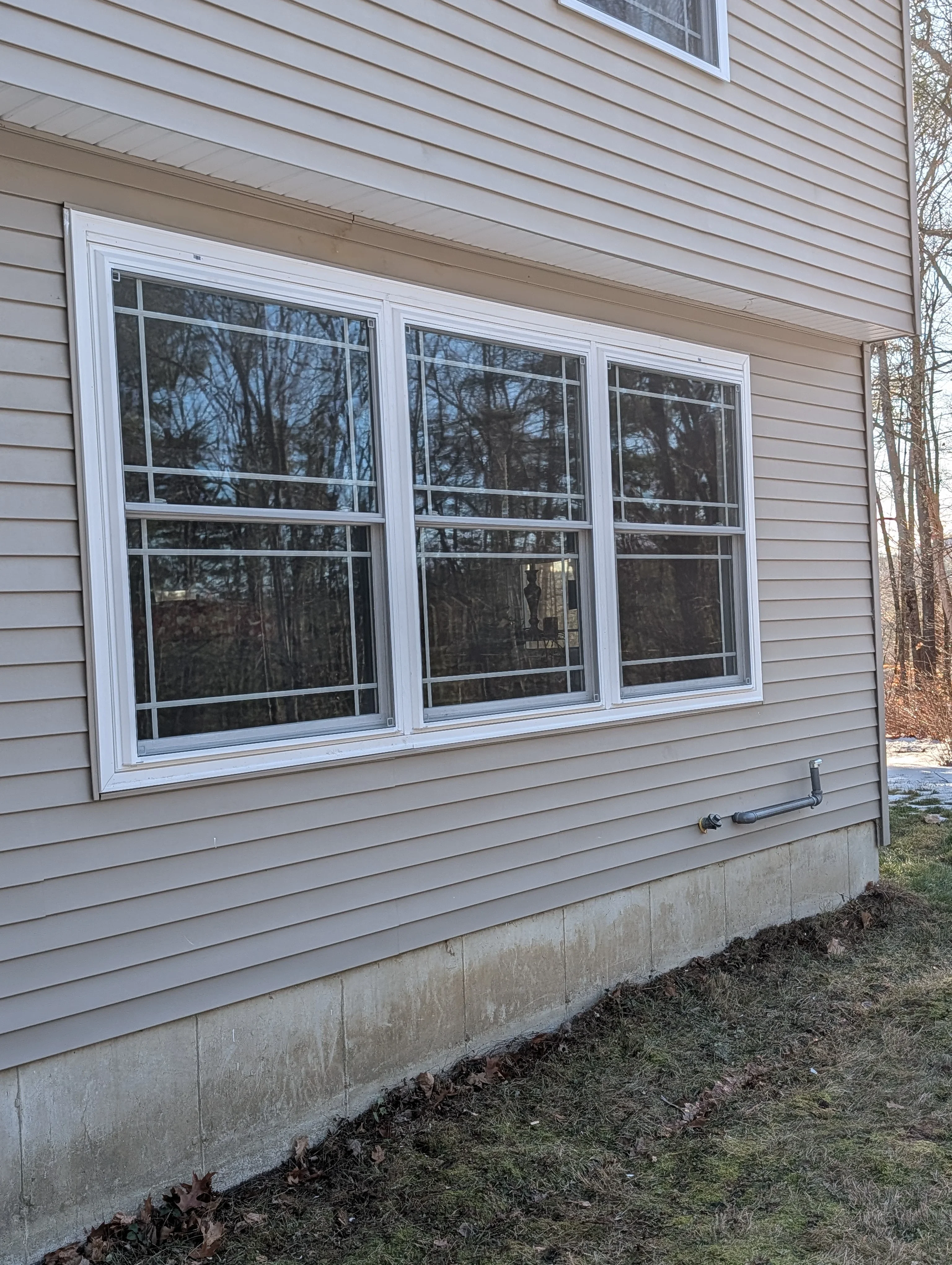 Three white double-hung windows installed on tan vinyl siding with gridded panes