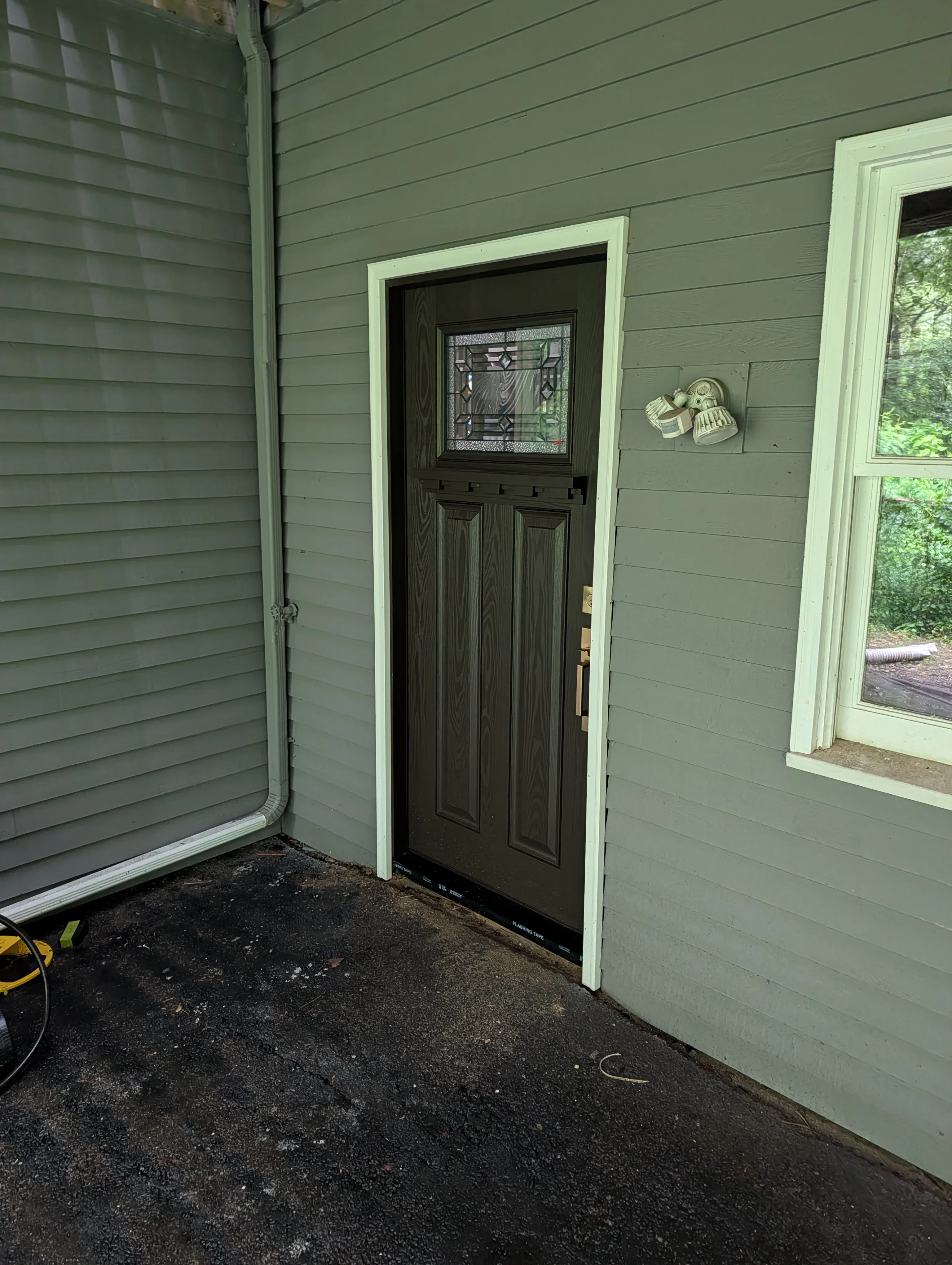 Sage green siding with dark wood entry door and white trim on residential exterior