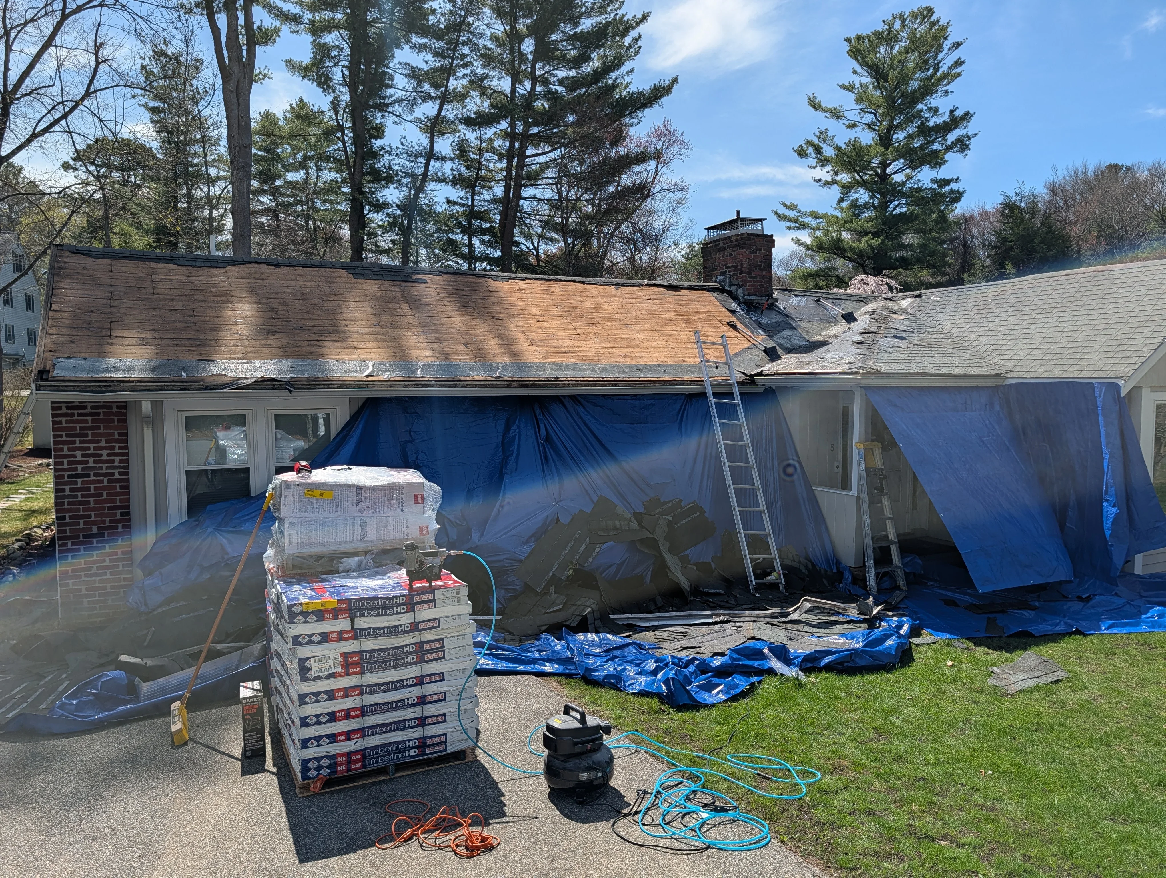 Residential roof replacement in progress with new shingles and protective tarping on brick home