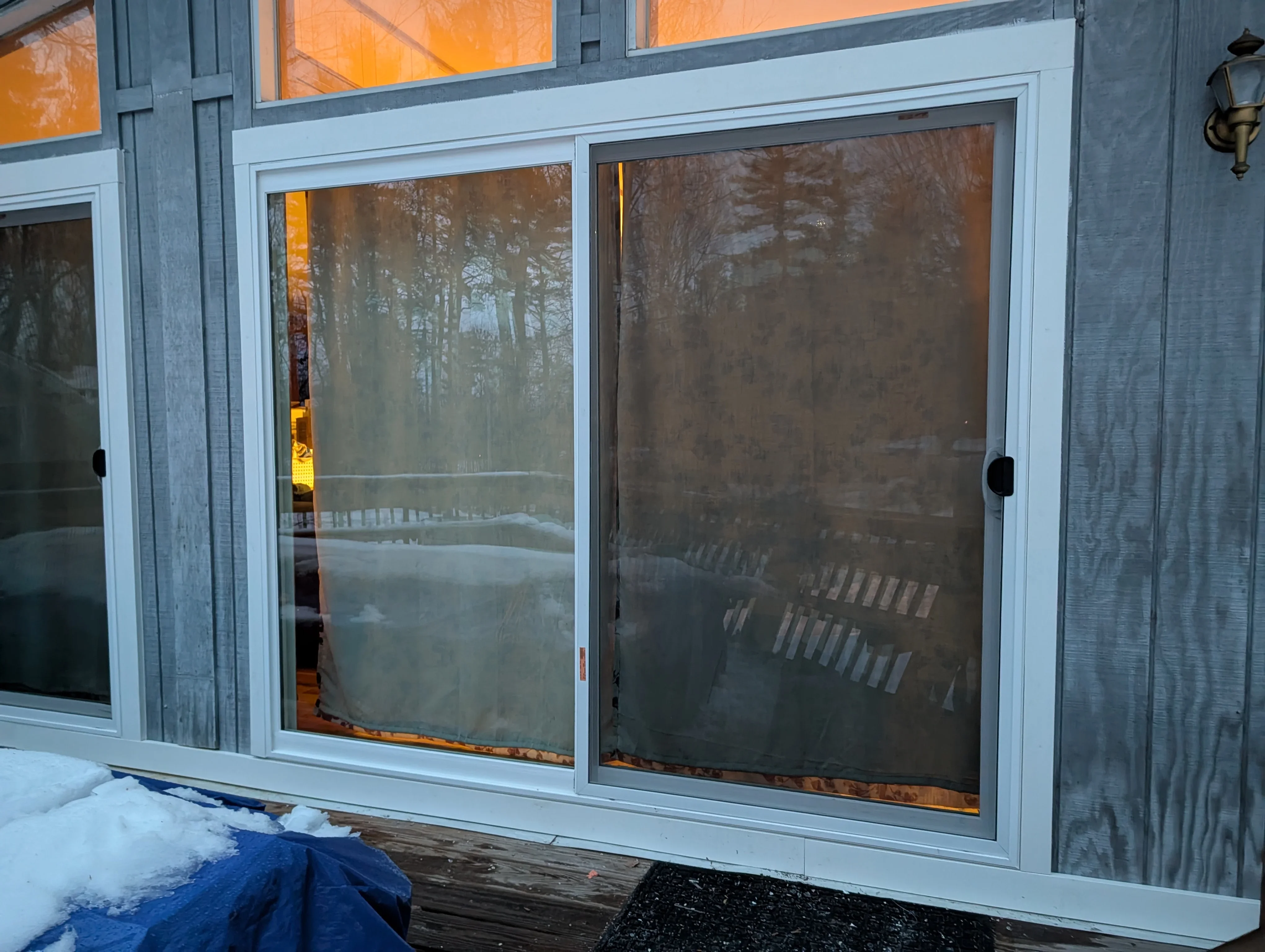 White sliding glass doors with screens installed on home exterior overlooking wooded area